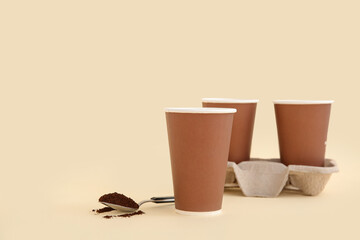 Brown takeaway paper cups with holder and beans on beige background