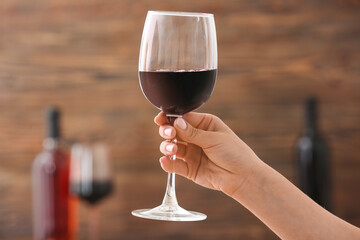 Female hand with glass of exquisite red wine on color background, closeup