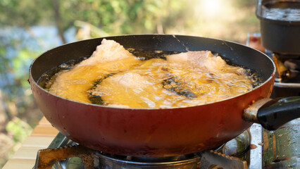 Abstract of Oil to cover the pork used for frying. In a pan, the inside is black and the outside is red. Cooking a picnic outside.