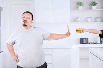 Overweight Asian guy refusing hamburger in the kitchen
