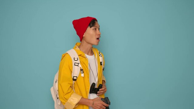 young asian tourist man looking through binoculars on blue background
