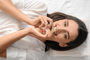 Obraz na płótnie Canvas Young woman eating cucumber slice in spa salon, top view
