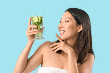 Young Asian woman with glass of cucumber water on blue background
