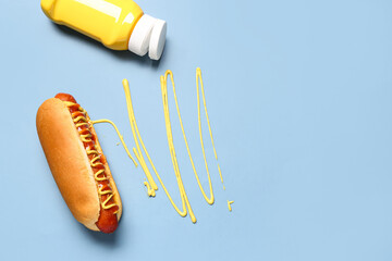 Tasty hot dog with bottle of mustard on blue background