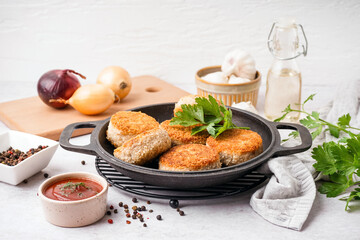 Frying pan with tasty meat cutlets and sauce on white background