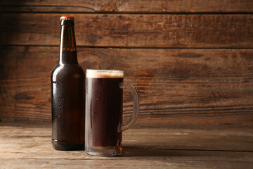Bottle and mug of dark beer on wooden background - obrazy, fototapety, plakaty