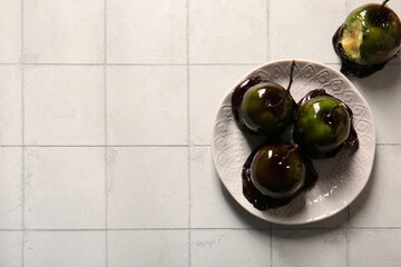 Tasty caramel apples for Halloween on white tile background