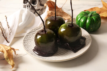 Plate of tasty caramel apples for Halloween on white marble background