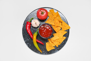 Board with tasty salsa sauce, nachos and ingredients on grey background