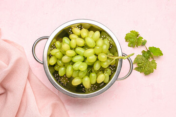 Sweet white grapes in a colander on color background, top view