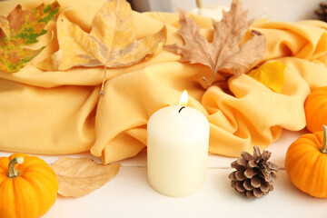 Obraz na płótnie Canvas Autumn leaves, burning candle, scarf, pine cone and pumpkins on white wooden background