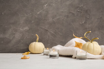 Cup of tea, burning candles, sweater, pumpkins and autumn leaves on table near grey wall