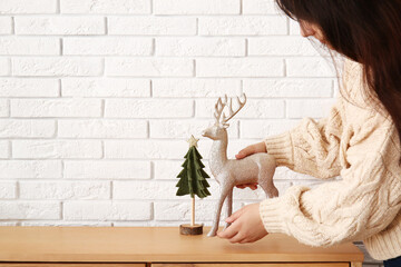 Woman decorating wooden cabinet with Christmas decorations near white brick wall