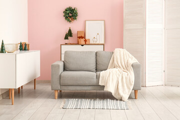 Interior of festive living room with grey sofa, blanket and Christmas decorations