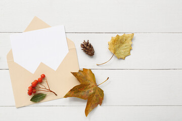 Envelope with blank card and autumn decor on white wooden background