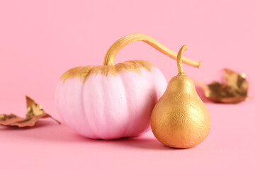 Painted pumpkin with golden pear and leaf on pink background