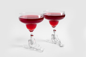 Glasses of delicious cocktail with skeletons for Halloween celebration on white background