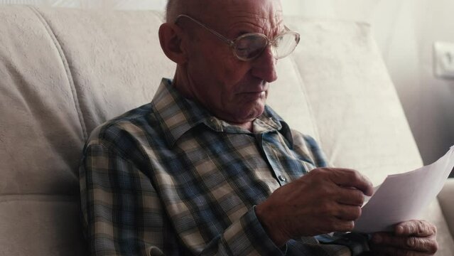 An elderly man sorts out mail and electricity bills. The pensioner is surprised by the increase in the cost of maintaining a house.