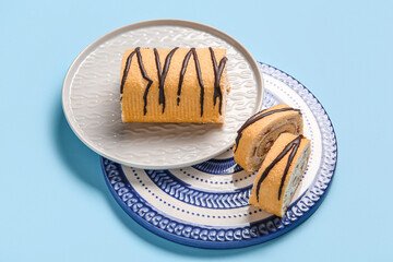 Plates with sweet sponge cake roll on blue background