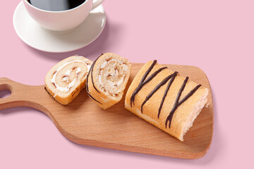 Wooden board with sweet sponge cake roll on pink background