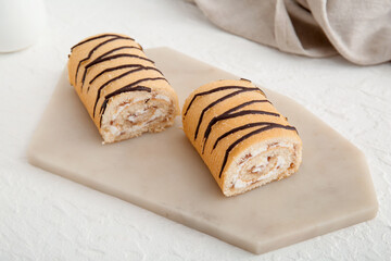 Board with halves of sweet sponge cake roll on white background