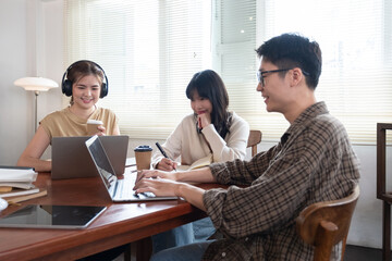 A group of cheerful Asian college students are enjoying talking and discussing their group project while sitting in a coffee shop together.