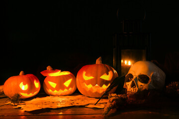 Halloween composition with jack-o-lanterns, skull and scroll on wooden table against black background