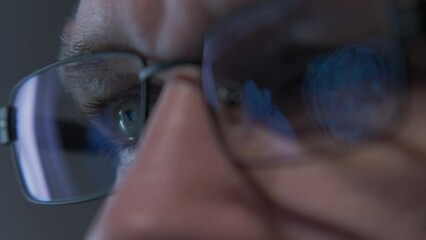 Male doctor eyes in eyeglasses late at night looking in front of MRI data on laptop. Close up