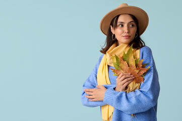 Beautiful young woman with autumn leaves on blue background