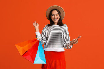 Beautiful young woman with shopping bags and mobile phone on red background