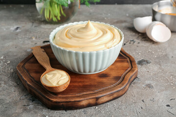 Bowl and spoon of fresh mayonnaise on grey background