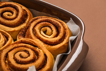 Baking dish of tasty cinnamon rolls on brown background
