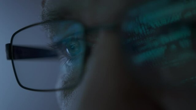 Close up shot of portrait of software engineer working on computer. Line of hack code run in reflection on eyeglasses 