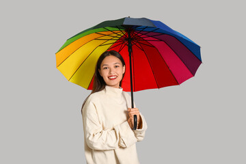 Beautiful young Asian woman with umbrella on grey background