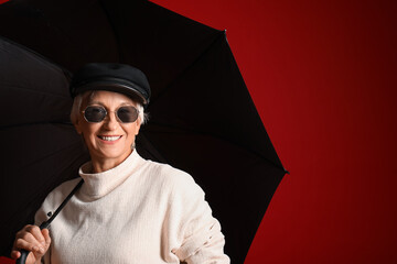 Beautiful mature woman with umbrella on red background