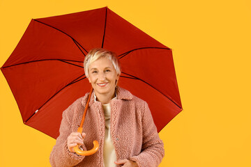 Beautiful mature woman with umbrella on yellow background