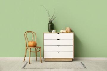 White chest of drawers and pumpkins, candles and tree branches near green wall