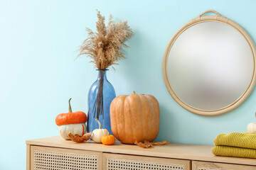 Wooden cabinet with pumpkins, pampas grass and mirror near blue wall