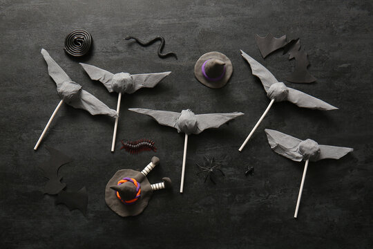 Sweet lollipops with liquorice, candy bugs and paper bats for Halloween party on black background