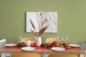 Autumn table setting with pumpkins, dry leaves and burning candles in dining room