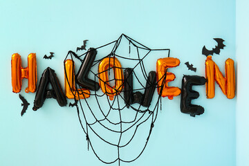 Word HALLOWEEN made of balloons with paper bats and web on blue wall