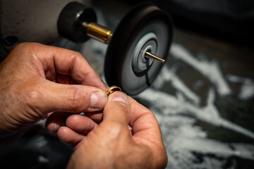 Goldsmith polishing a gold ring jewel in his jewelry workshop. Jeweler hands working in his...