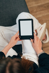 Young woman sitting the couch with an e-book