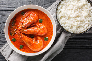 Chingri malai curry also known as prawn malai curry made from tiger and king prawns and coconut milk and flavoured with spices closeup on the wooden table. Horizontal top view from above