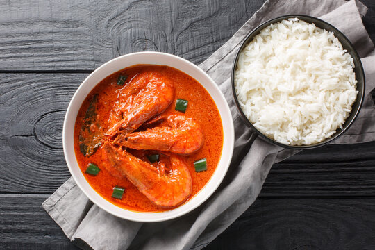 Malai curry dish combines prawns with coconut milk, onion, ginger, garlic paste, tomato, and ground spices and is served with basmati rice closeup on the wooden table. Horizontal top view from above