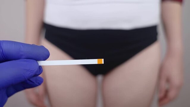 Bacterial Vaginosis. Vaginal pH. Girl shows sticks for measuring acid-base balance of genital organs. Self-diagnosis. Normal acidity level shown in colors and must be compared with the standard