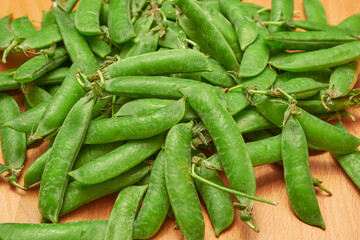green ripe plucked pea pods on a wooden kitchen cutting board close-up