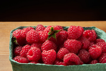 delicious fresh raw red raspberries in natural eco-friendly packaging in a green cardboard basket on a wooden table close-up. harvest. healthy food. diet. summer. vitamins