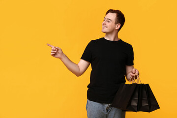 Young man with shopping bags pointing at something on yellow background. Black Friday sale