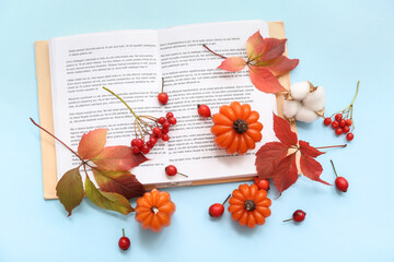 Beautiful composition with candles in shape of pumpkin, book and autumn leaves on blue background